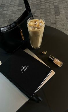 a table with a book, coffee and a purse on it next to a drink