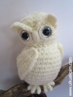 a crocheted white owl sitting on top of a tree branch with big eyes