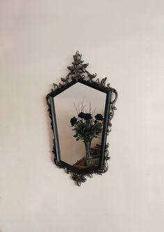 a mirror hanging on the side of a wall with flowers in it and a vase