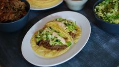 three tacos are sitting on a plate next to bowls of salad and coleslaw