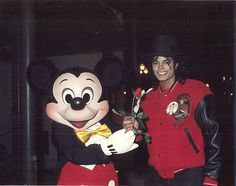 a man standing next to mickey mouse holding a rose