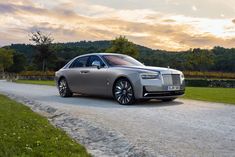 a silver rolls royce parked on the side of a road in front of some trees