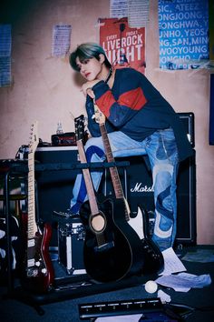 a young man sitting on top of a guitar case next to other guitars and amps