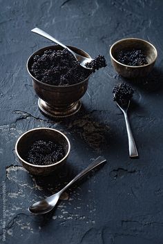 two bowls filled with black cavia on top of a table next to spoons