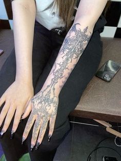 a woman sitting on top of a wooden table with her arm covered in tattoos and nails