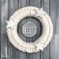 a white rope wreath with silver stars hanging from it's side on a wooden wall