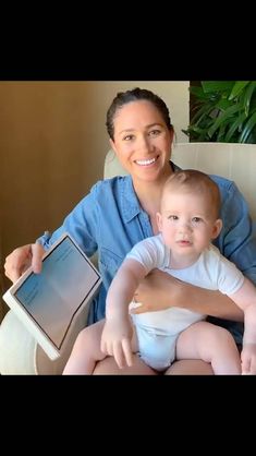 a woman holding a baby while sitting on top of a white couch next to a potted plant