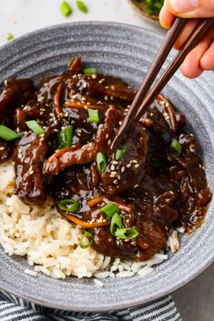 someone is holding chopsticks over rice with beef and sauce on the side in a bowl