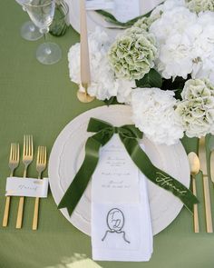 the table is set with white flowers and green napkins, gold cutlery, and silverware