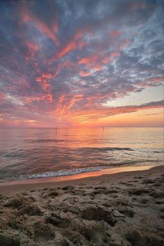 the sun is setting over the ocean with sailboats in the distance and sand on the beach