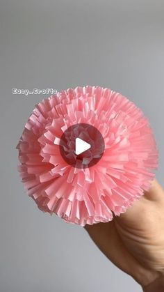 a hand holding a pink paper flower with a video in the middle