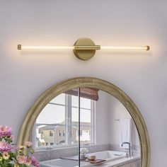 a bathroom mirror with a light on above it and flowers in front of the mirror