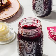 two jars filled with jam sitting on top of a table next to plates and cups