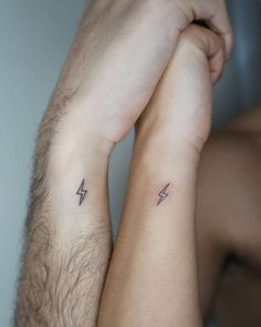 two people holding hands with tattoos on their arms and one has a small lightning tattoo on the wrist