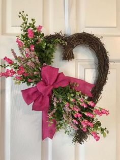 a heart - shaped wreath with pink flowers and greenery hangs on the front door