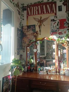 a desk with many items on it in front of a mirror and wall covered with posters