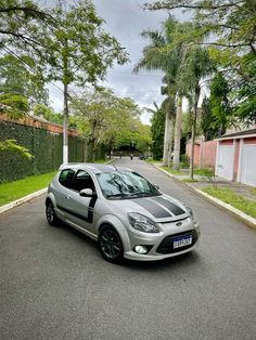 a small silver car parked on the side of a road next to a tree lined street