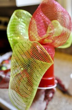 a red vase with green and pink ribbons on top of it, sitting on a counter