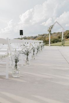 rows of white chairs lined up with flowers in vases