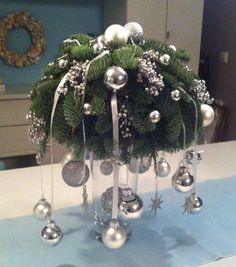 a christmas centerpiece on a table with silver balls and greenery hanging from it