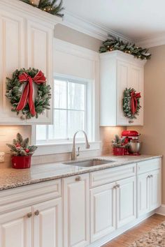 a kitchen decorated for christmas with wreaths on the cabinets