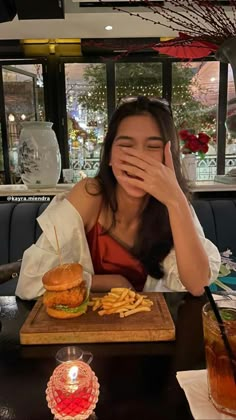 a woman sitting at a table with a hamburger and fries in front of her face