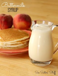 a plate topped with pancakes and a glass of milk next to two peaches on a table