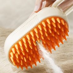 an orange and white hair brush being held by someone's hand with water coming out of it