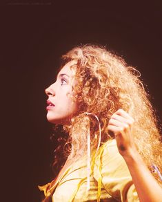 a woman with long curly hair is holding her hand up to her ear and looking off into the distance