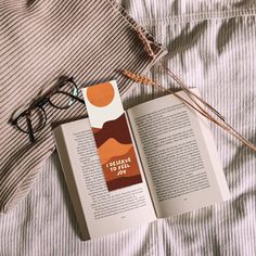 an open book on top of a bed next to reading glasses