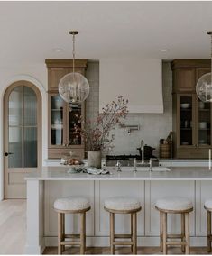 a kitchen with white counter tops and stools in front of an island that has three lights hanging from it