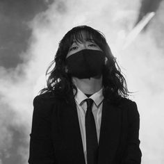 a man with long hair wearing a suit and tie, covering his face with a mask