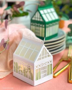 a small white house sitting on top of a table next to plates and cups with gold forks