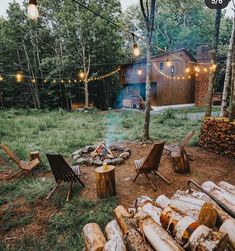 an outdoor fire pit surrounded by chairs and logs with lights strung from the trees around it