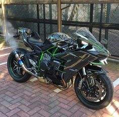 a black motorcycle parked on top of a brick road next to a metal fence and gate