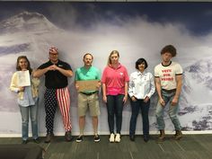 a group of people standing next to each other in front of a wall with mountains on it