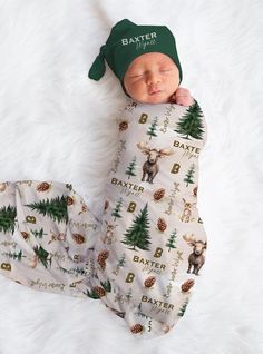 a baby is sleeping on a white blanket wearing a green hat and deer print pants