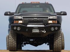 the front end of a black truck on dirt road with blue sky in back ground