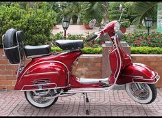 a red scooter is parked in front of a brick wall and flowerbeds