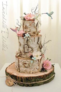 a three tiered wedding cake decorated with flowers and hearts on a tree stump stand