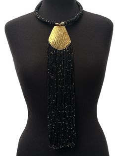 This stunning necklace has been made using authentic brass and features beautiful black beads, creating a striking piece with an ethnic feel. The pendant is delicately engraved with intricate details, and the fringe adds a touch of movement to the design. The necklace is perfect for women who love unique and eye-catching jewellery. Its African origins and cultural significance make it an ideal addition to any collection, and it will add a touch of style and elegance to any outfit.
Material: Bead Elegant Beaded Fringe Jewelry For Festivals, Gold Jewelry With Beaded Fringe For Festival, Black Artisan Beaded Chain Jewelry, Artisan Black Beaded Chain Jewelry, Traditional Black And Gold Beads, Artisan Black Beaded Necklaces With Adjustable Fit, Artisan Black Adjustable Beaded Necklaces, Artisan Black Beaded Chain, Artisan Black Necklace With Beaded Chain