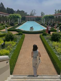 a woman walking up some steps towards a pool in the middle of a formal garden