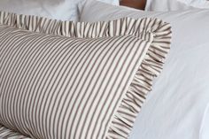 a close up of a pillow on a bed with white linens and brown stripes