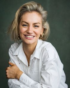 a woman with blonde hair smiling at the camera while wearing a white shirt and gold hoop earrings