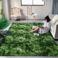 a woman sitting on top of a green rug in a living room next to a couch