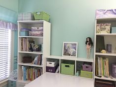 a room with several shelves filled with books and dolls on top of each bookcase