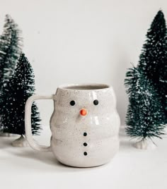 a ceramic mug with a snowman face on it and trees in the back ground