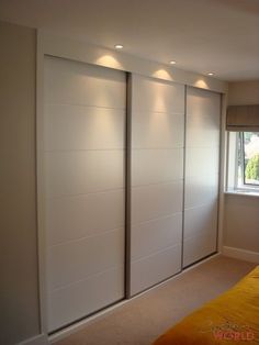 an empty bedroom with white sliding doors and yellow sheets on the bed, in front of a window