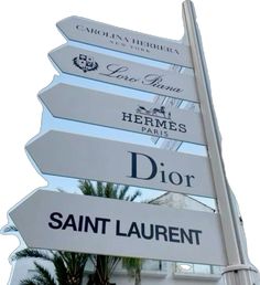 a white street sign with many different signs on it's side and palm trees in the background