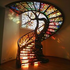 a spiral staircase in front of a stained glass window with a tree on the top